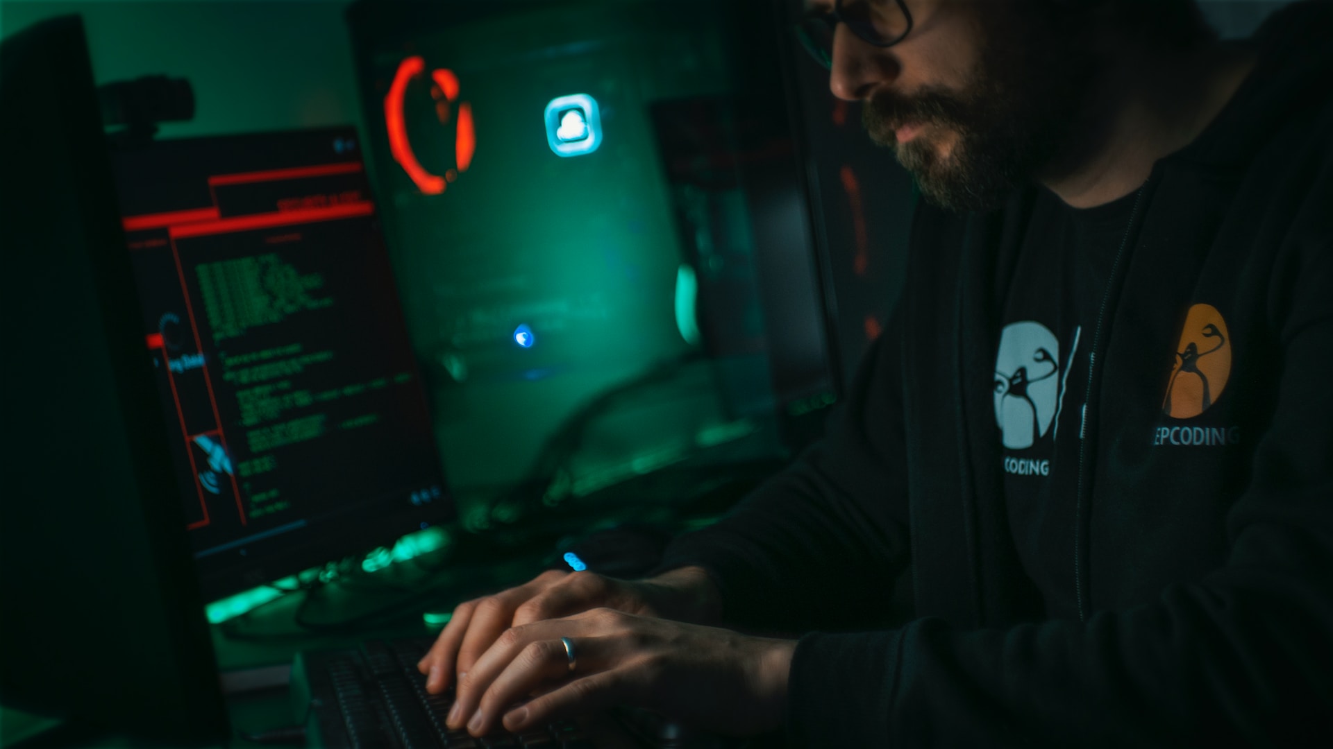 Man in a dark room coding on multiple computers for cybersecurity for businesses